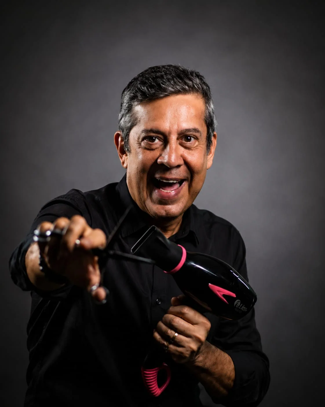 Edu Domingos apontando um secador para a câmera, sorrindo